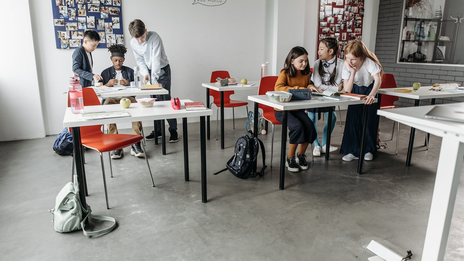 A classroom of separated desks with students working in small groups and bags stowed underneath