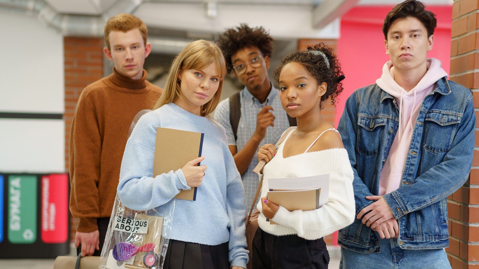 Five sixth-form students standing together in a college corridor holding notebooks and folders