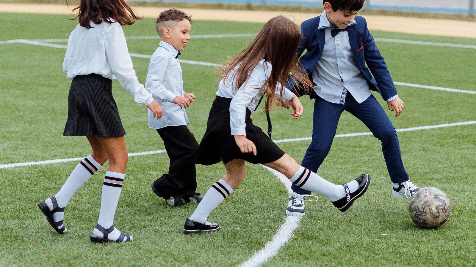 Primary school children in uniform playing football together on a grass pitch