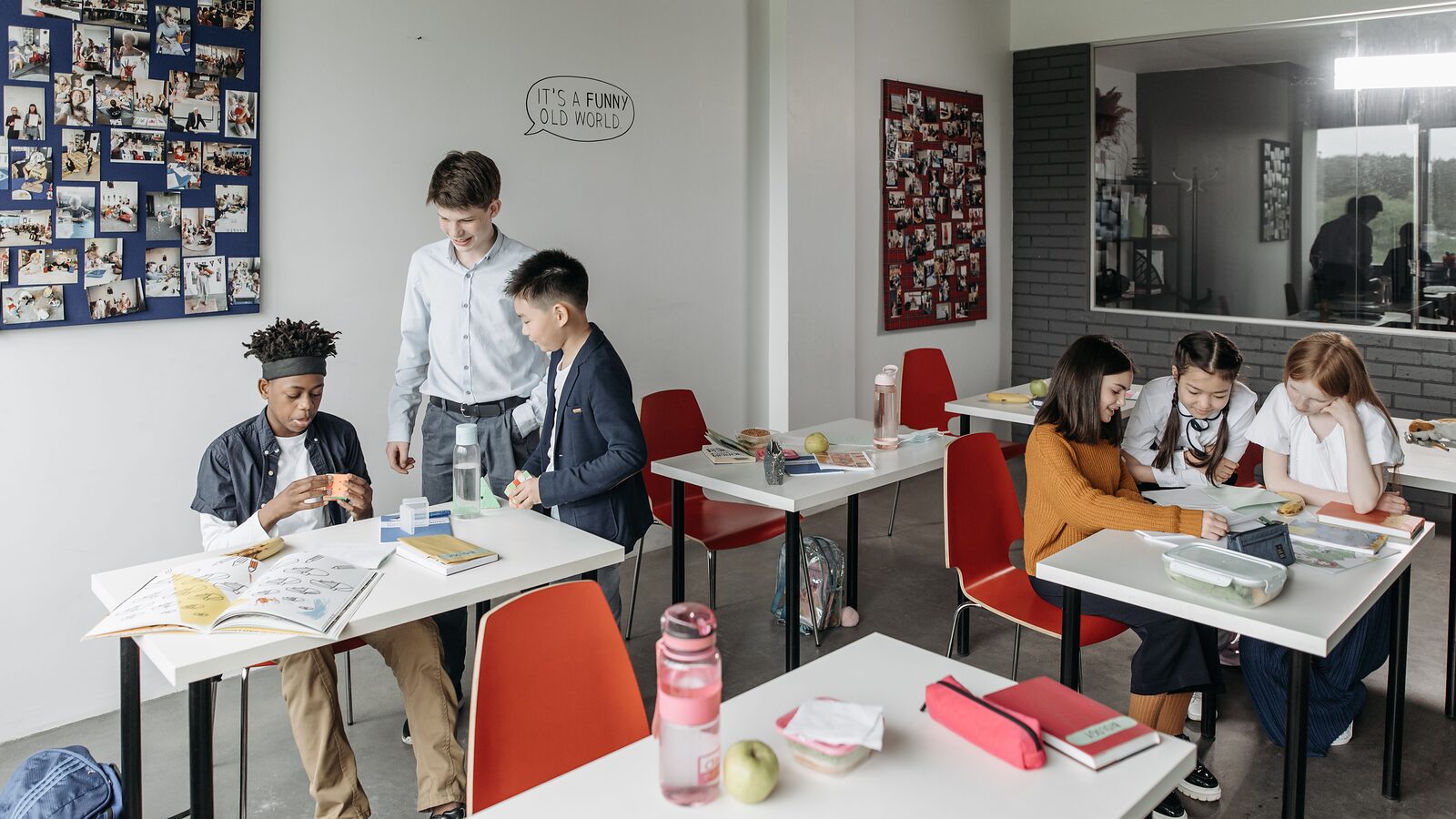 Pupils working at classroom desks with open books, pencil cases and lunch boxes spread out in front of them