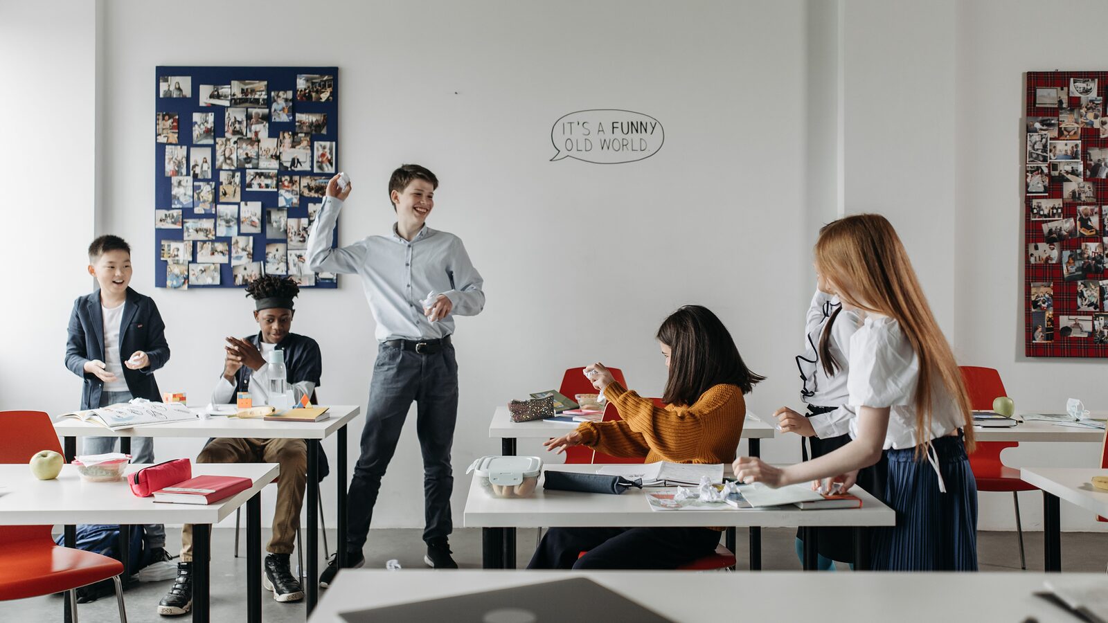 Pupils moving between desks in a classroom at break, books and lunch boxes left out on the tables